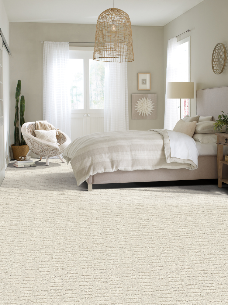carpet in bedroom, plant in corner, chair next to plant, bed with off white sheets